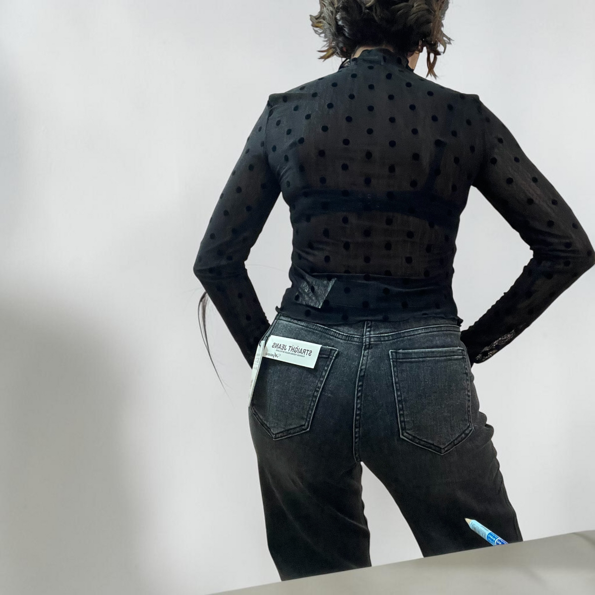 Modella indossa una blusa Caldea Boutique nera a maniche lunghe con collo alto e motivo a pois in rilievo