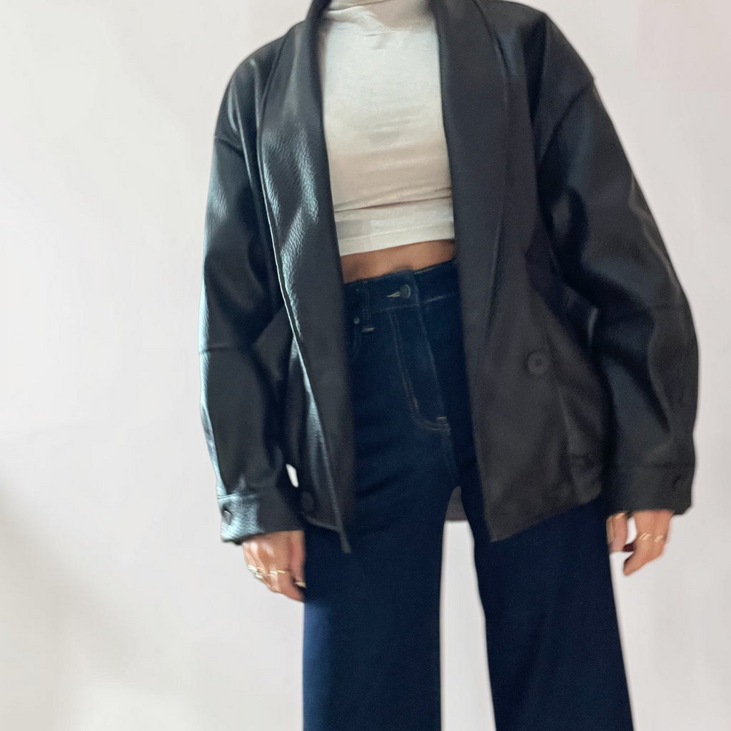Modella indossa giacca bomber oversize nera in ecopelle di Caldea Boutique con top bianco e jeans a gamba larga