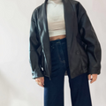 Modella indossa giacca bomber oversize nera in ecopelle di Caldea Boutique con top bianco e jeans a gamba larga