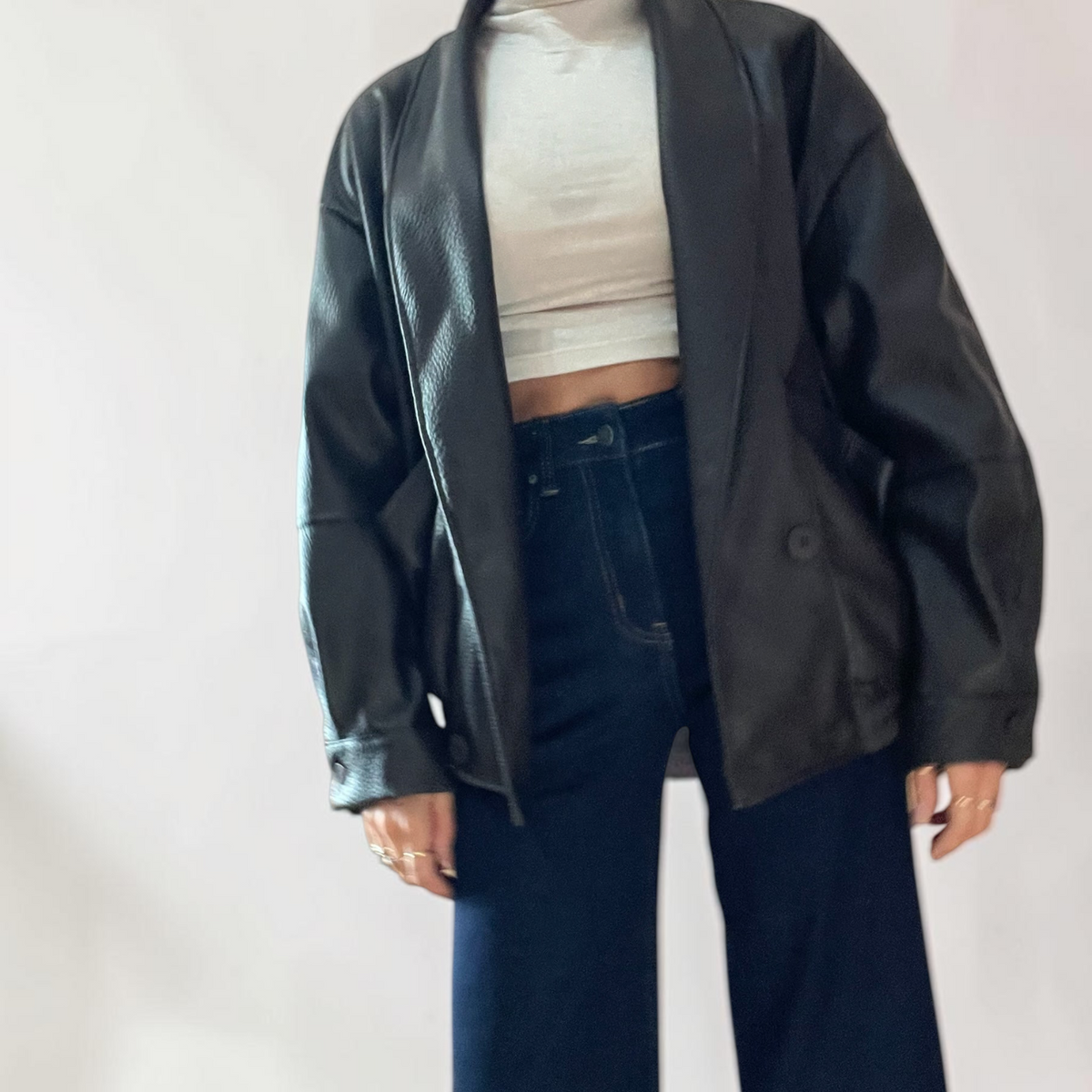 Modella indossa giacca bomber oversize nera in ecopelle di Caldea Boutique con top bianco e jeans a gamba larga