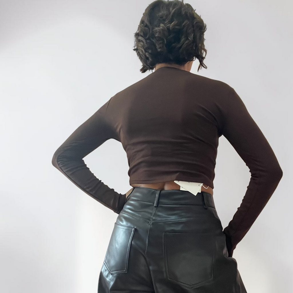Modella di spalle indossa maglia crop a maniche lunghe marrone Caldea Boutique con pantaloni neri in ecopelle