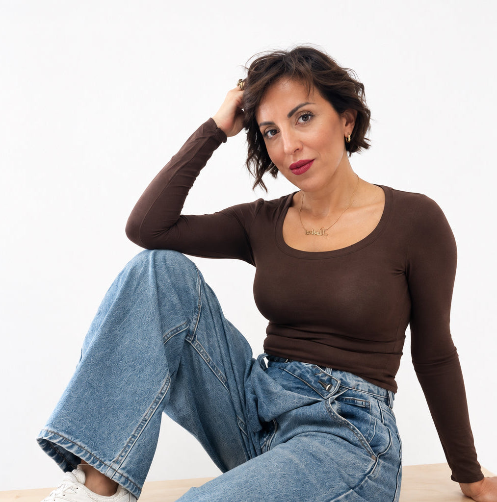 Modella seduta indossa una maglia a maniche lunghe Caldea Boutique color testa di moro con jeans e sneakers bianche